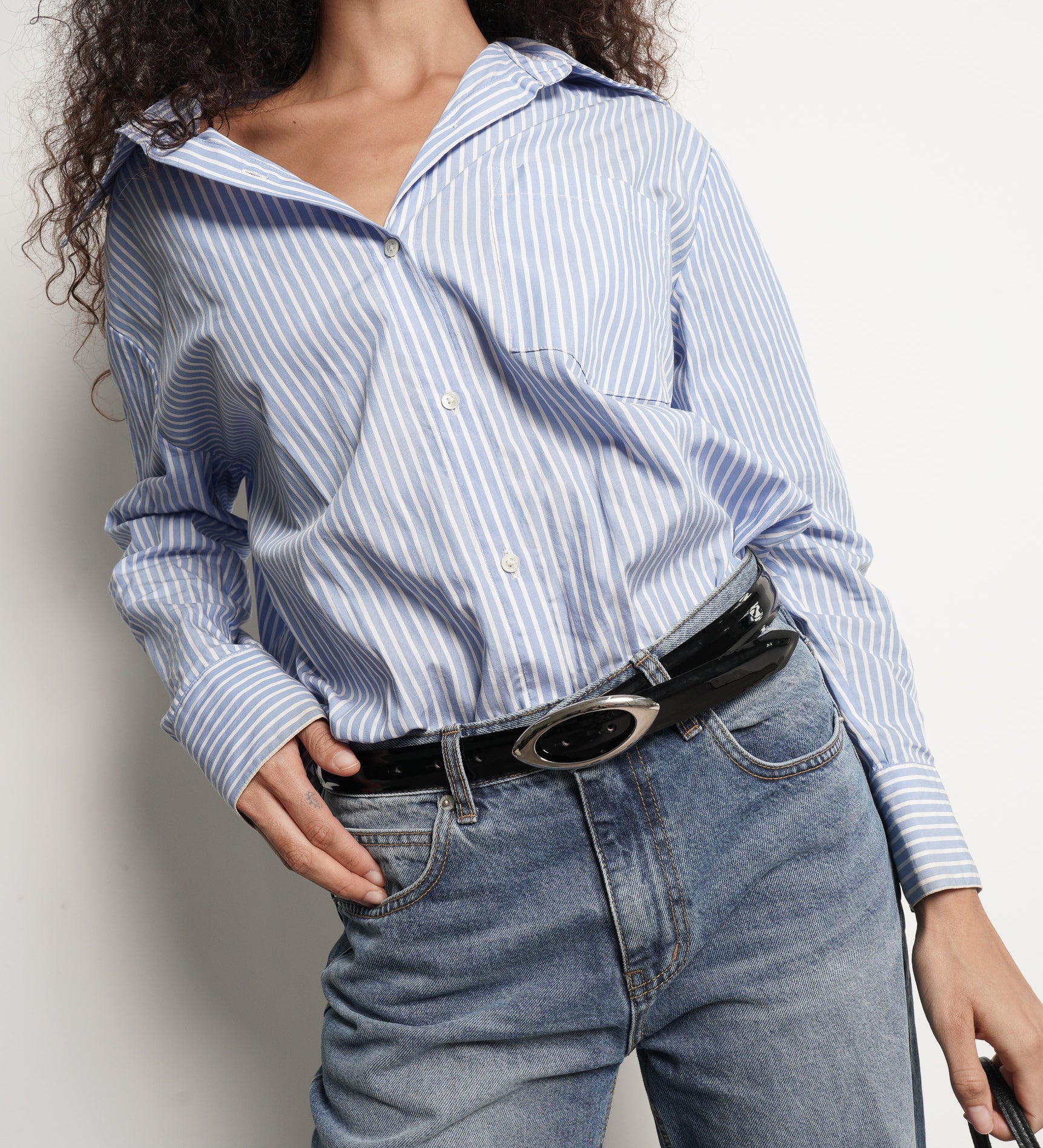 Person wearing a blue and white striped shirt and jeans with a black patent leather belt - Streets Ahead