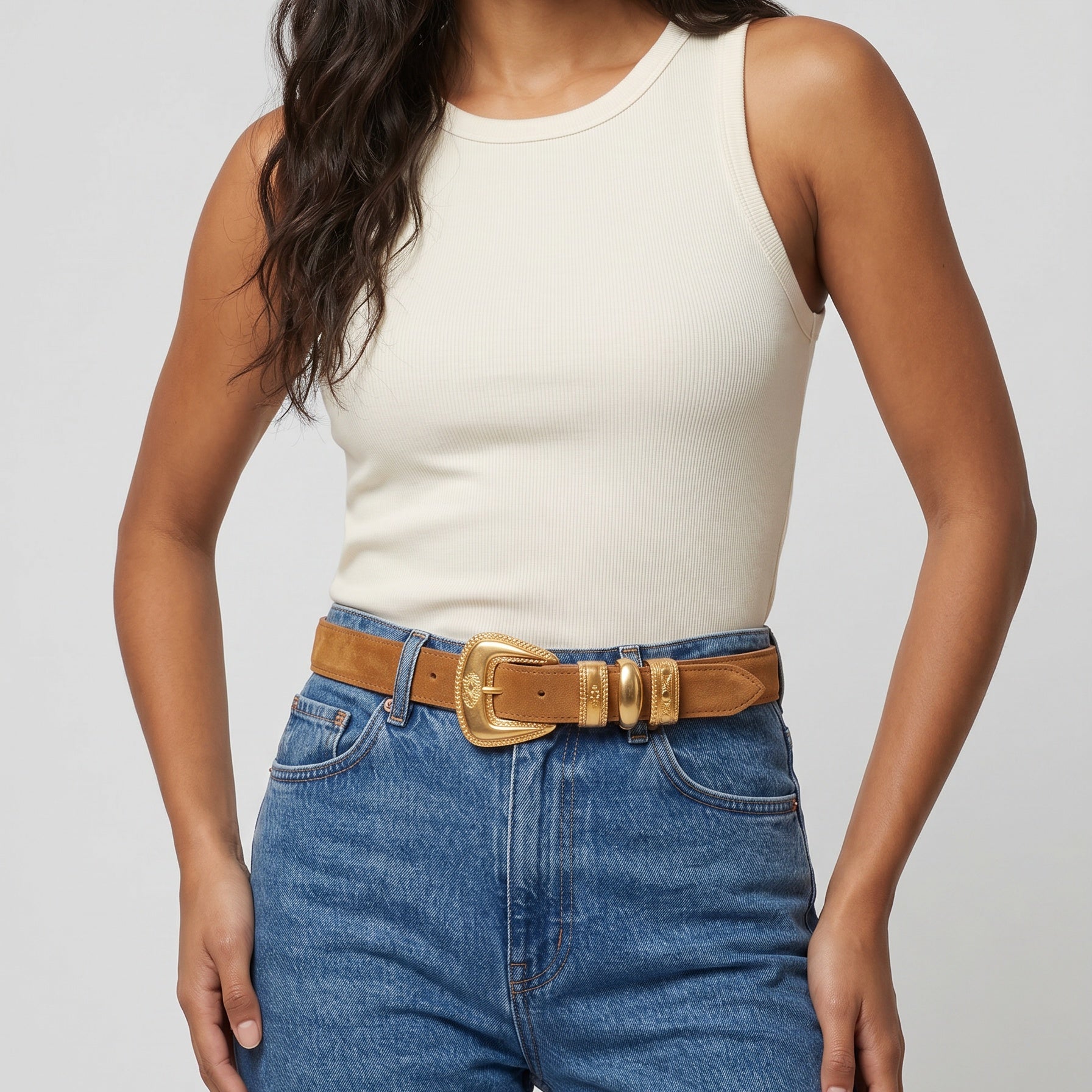 Woman wearing a white tank top and blue jeans with a brown belt on a light gray background