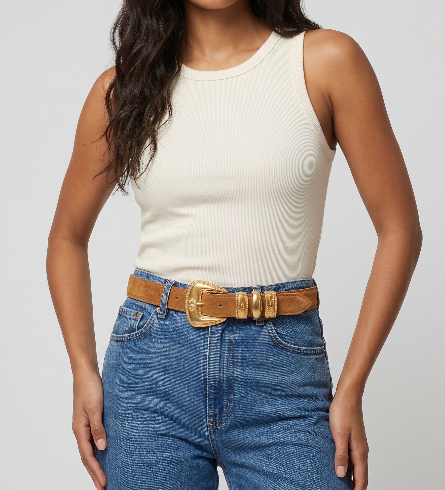Woman wearing a white tank top and blue jeans with a brown belt on a light gray background