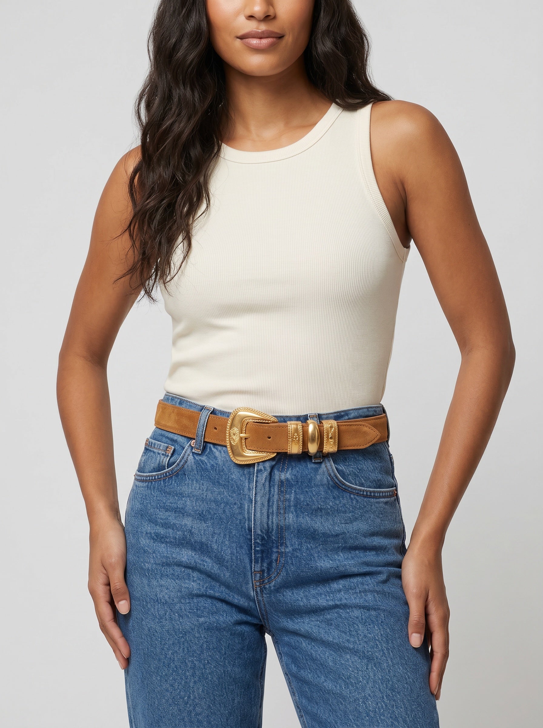 Woman wearing a white tank top and blue jeans with a brown belt on a light gray background