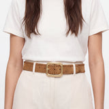Person wearing a white t-shirt and beige pants with a brown belt on a plain background