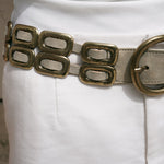Close up of the Saskia Belt brass buckle and oval brass hardware woven through shimmer ivory leather