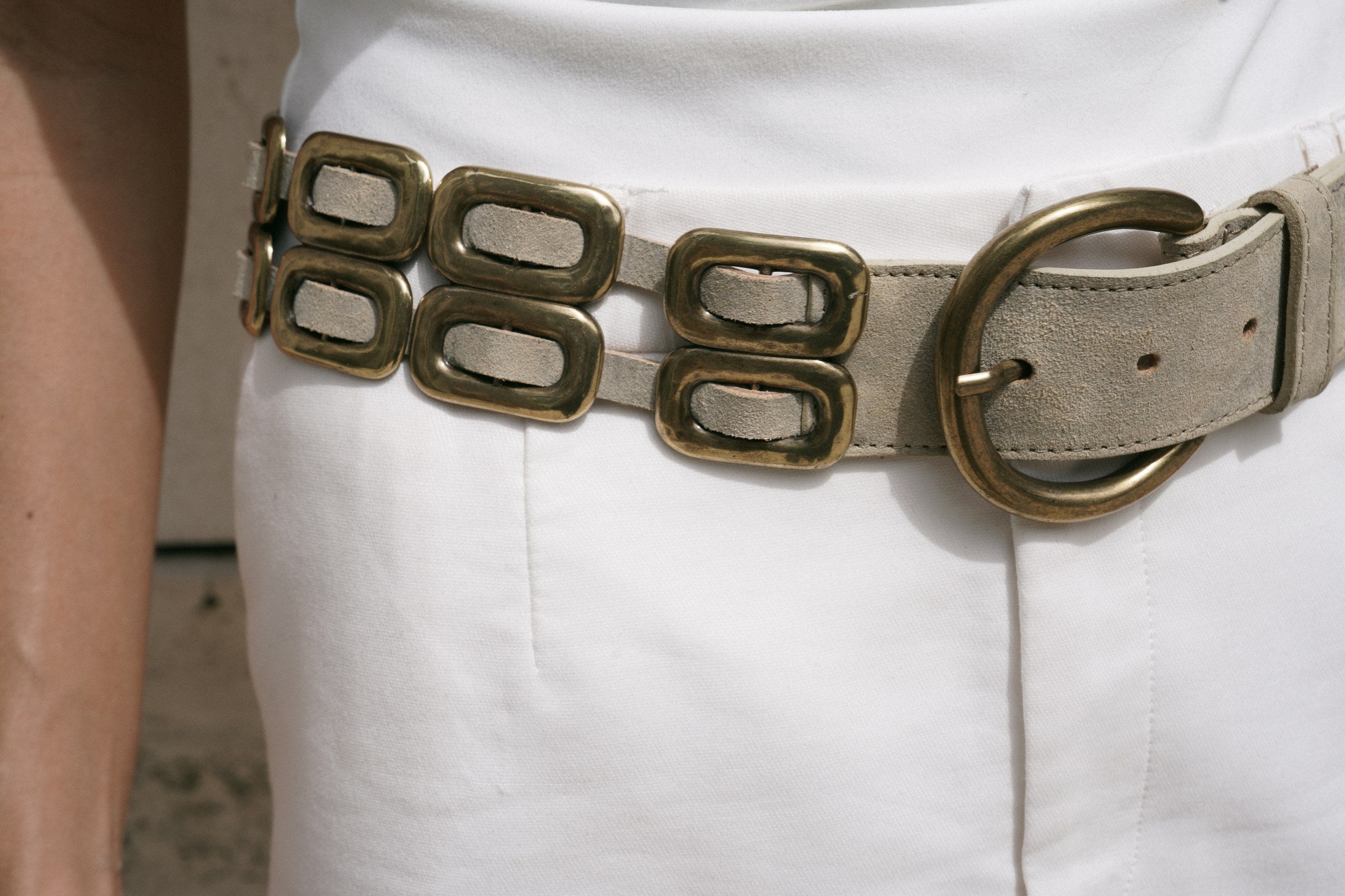 Close up of the Saskia Belt brass buckle and oval brass hardware woven through shimmer ivory leather